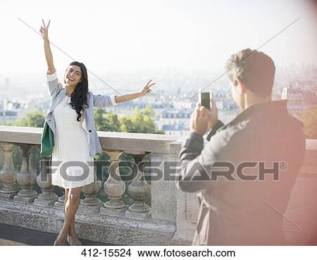 Picture - Man photographing girlfriend with city in background. Fotosearch