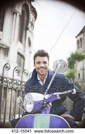Stock Image - Man sitting on scooter on urban street. Fotosearch