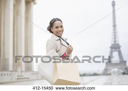 Stock Image - Woman carrying shopping bags near Eiffel Tower, Paris, France. Fotosearch