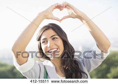 Stock Image - Woman making heart-shape with hands outdoors. Fotosearch