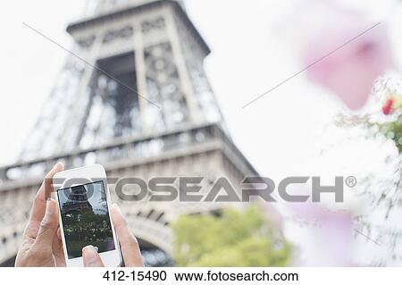 Stock Image - Woman photographing Eiffel Tower with camera phone, Paris, France. Fotosearch