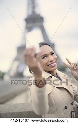 Stock Photo - Woman taking picture in front of Eiffel Tower, Paris, France. Fotosearch