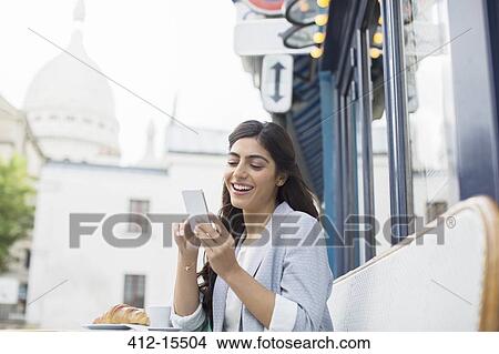 Picture - Woman using cell phone at sidewalk cafe near Sacre Coeur Basilica, Paris, France. Fotosearch