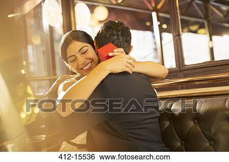 Stock Photograph - Woman with jewelry box hugging man in restaurant. Fotosearch