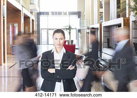 Stock Image - Businesswoman standing in bustling lobby. Fotosearch