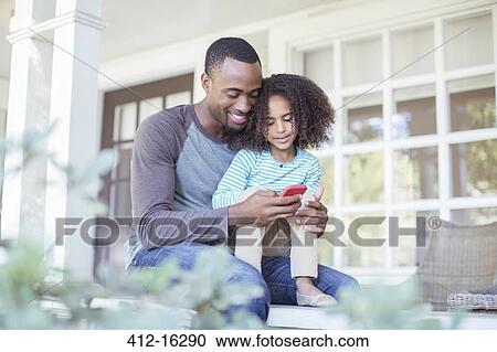 Stock Image - Father and daughter using cell phone on porch. Fotosearch