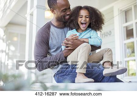 Stock Photo - Father tickling daughter on porch. Fotosearch