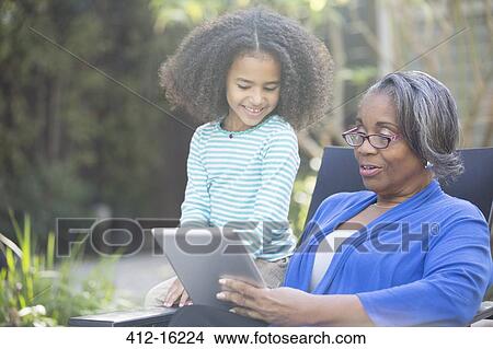 Picture - Grandmother and granddaughter using digital tablet outdoors. Fotosearch