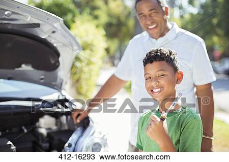 Stock Image - Portrait of smiling grandson repairing car engine with grandfather. Fotosearch