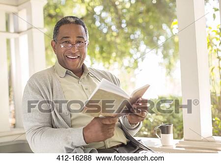Stock Photo - Portrait of smiling senior man reading book on porch. Fotosearch