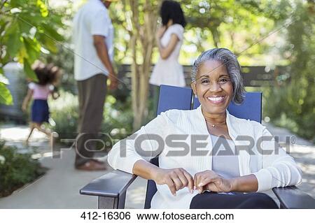 Stock Photograph - Portrait of smiling senior woman on patio with family in background. Fotosearch