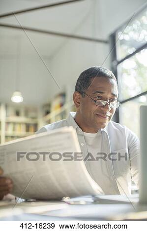 Senior man reading newspaper and using laptop View Large Photo Image Stock Photo - Senior man reading newspaper and using laptop. Fotosearch