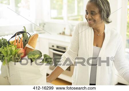 Stock Photo - Smiling senior women with groceries in kitchen. Fotosearch