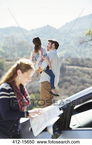 Stock Image - Father holding daughter at roadside while woman checks map. Fotosearch