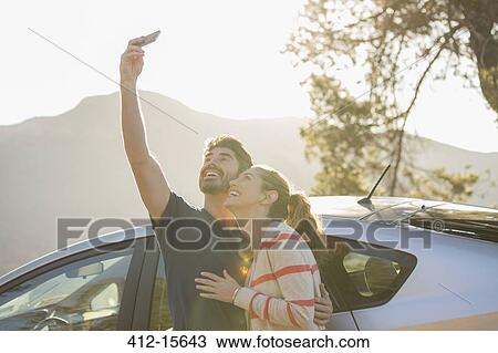 Happy couple taking self-portrait with camera phone outside car View Large Photo Image Stock Image - Happy couple taking self-portrait with camera phone outside car. Fotosearch
