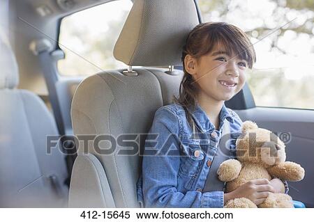 Stock Photography - Happy girl with teddy bear in back seat of car. Fotosearch