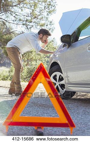 Stock Photograph - Man at roadside checking car engine behind warning triangle. Fotosearch