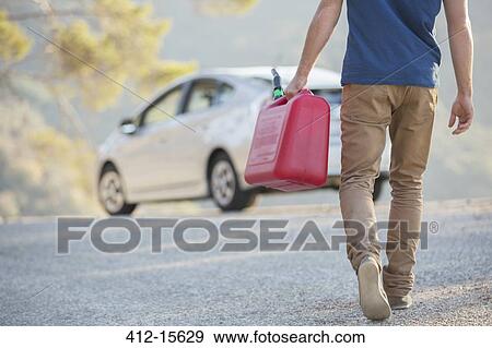 Stock Photo - Man carrying gas can to car at roadside. Fotosearch