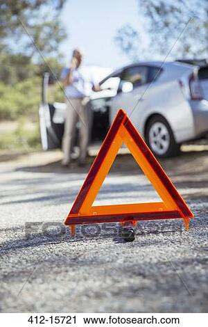 Stock Image - Man talking on cell phone at roadside behind warning triangle. Fotosearch