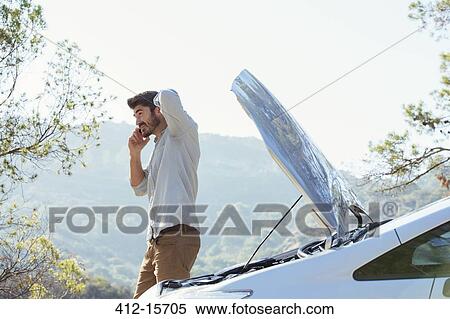 Stock Photography - Man talking on cell phone with automobile hood raised at roadside. Fotosearch