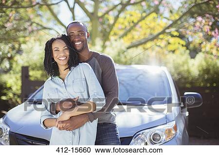 Stock Image - Portrait of happy couple hugging outside car. Fotosearch