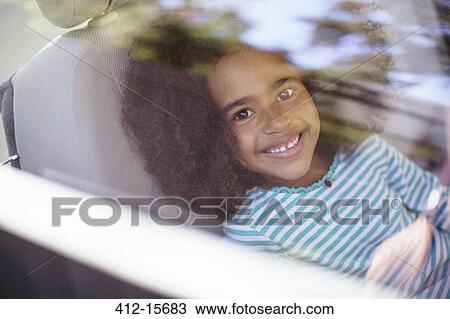 Stock Image - Portrait of happy girl in back seat of car. Fotosearch