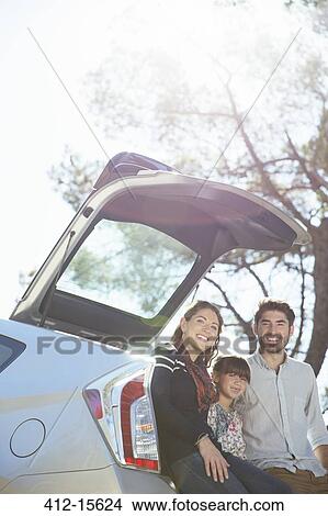 Portrait of smiling family sitting against rear of car View Large Photo Image Picture - Portrait of smiling family sitting against rear of car. Fotosearch