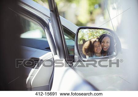 Stock Image - Reflection of smiling mother and daughter in side-view mirror. Fotosearch