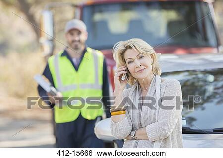 Stock Photograph - Roadside mechanic behind woman on cell phone. Fotosearch