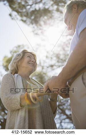 Stock Image - Senior couple holding hands under trees. Fotosearch