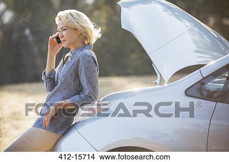 Woman talking on cell phone with automobile hood raised at roadside View Large Photo Image Picture - Woman talking on cell phone with automobile hood raised at roadside. Fotosearch