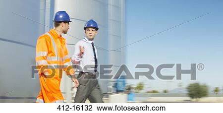 Stock Image - Businessman and worker talking near silage storage towers. Fotosearch