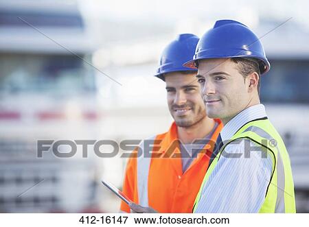 Stock Photo - Businessman and worker using digital tablet near trucks. Fotosearch