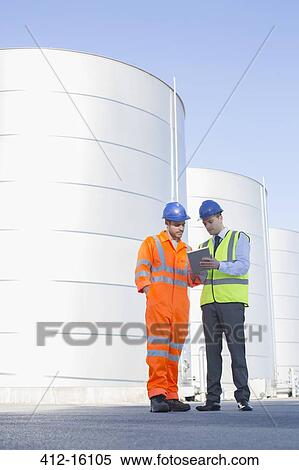 Stock Photography - Businessman and worker using digital tablet next to silage storage towers. Fotosearch