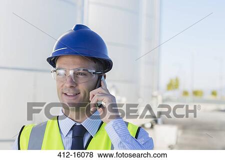 Stock Photo - Close up of worker talking on cell phone in front of silage storage tower. Fotosearch