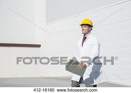 Stock Image - Scientist in hard-hat with clipboard walking outdoors. Fotosearch