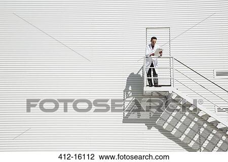 Stock Image - Scientist standing on sunny platform against building. Fotosearch