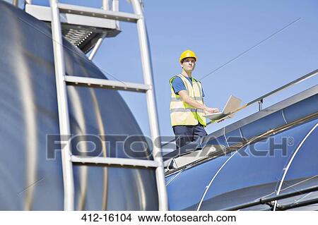 Worker using laptop on platform above stainless steel milk tanker View Large Photo Image Picture - Worker using laptop on platform above stainless steel milk tanker. Fotosearch