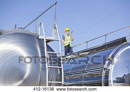 Stock Photo - Worker using walkie-talkie on platform above stainless steel milk tanker. Fotosearch