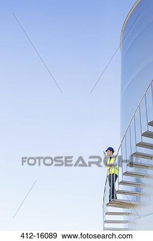 Stock Photo - Worker using walkie-talkie on winding steps along silage storage tower. Fotosearch