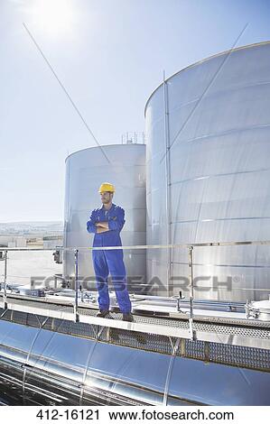 Stock Image - Worker with arms crossed on platform above stainless steel milk tanker. Fotosearch