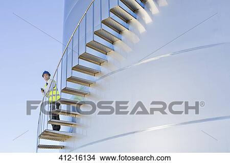 Worker with walkie-talkie standing on stairs winding along silage storage tower View Large Photo Image Picture - Worker with walkie-talkie standing on stairs winding along silage storage tower. Fotosearch
