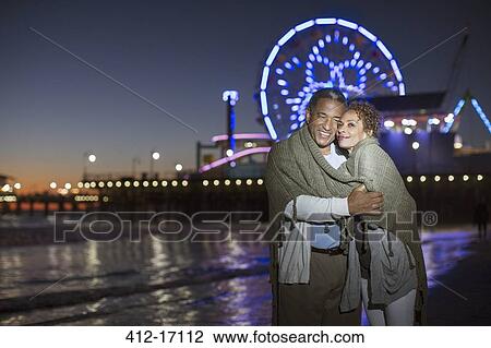 Stock Image - Couple hugging on beach at night. Fotosearch