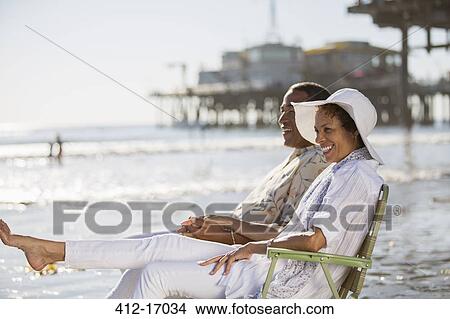 Picture - Couple relaxing in lawn chairs on beach. Fotosearch