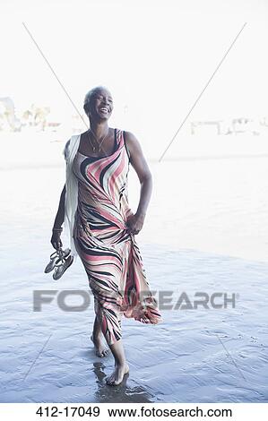 Stock Photo - Happy woman in dress walking barefoot on beach. Fotosearch