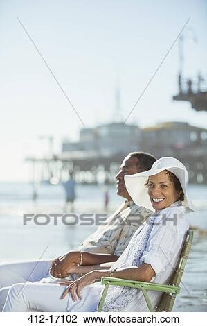 Portrait of couple relaxing in lawn chairs on sunny beach View Large Photo Image Stock Image - Portrait of couple relaxing in lawn chairs on sunny beach. Fotosearch