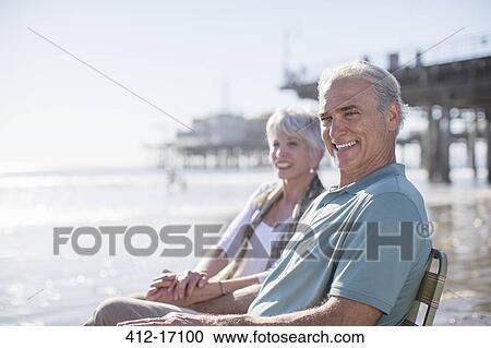 Stock Image - Portrait of senior couple relaxing on sunny beach. Fotosearch