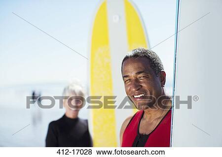 Stock Photo - Portrait of senior couple with surfboards on beach. Fotosearch