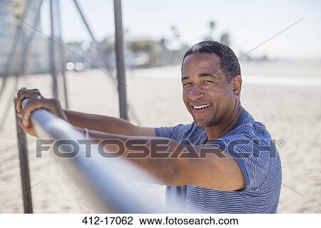 Stock Image - Portrait of senior man leaning on bar at beach playground. Fotosearch