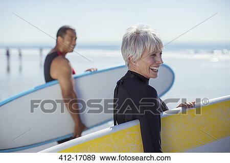 Stock Photo - Senior couple carrying surfboards on beach. Fotosearch